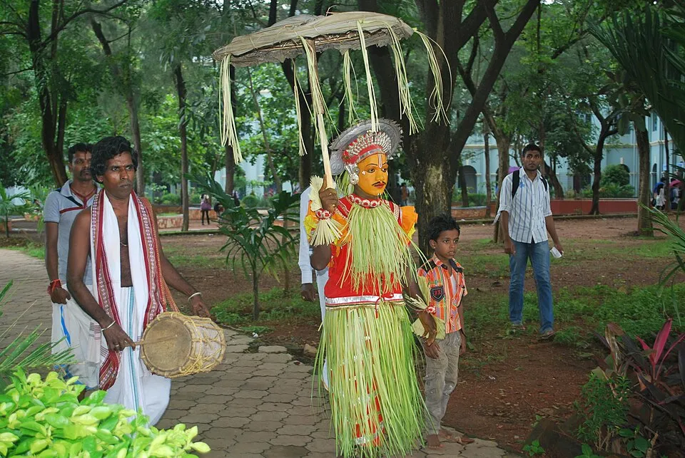 An Aati Kalenja performer with a painted face, a skirt of coconut fronds and an umbrella of dry palm leaves, walking beside a drummer with a tembere