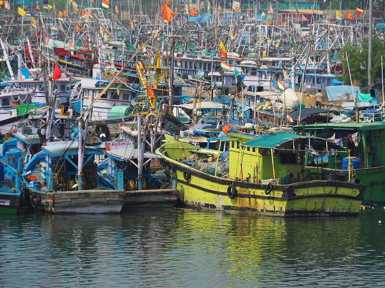 Brightly painted wooden fishing boats crowded together in the harbour at Malpe, flying small flags