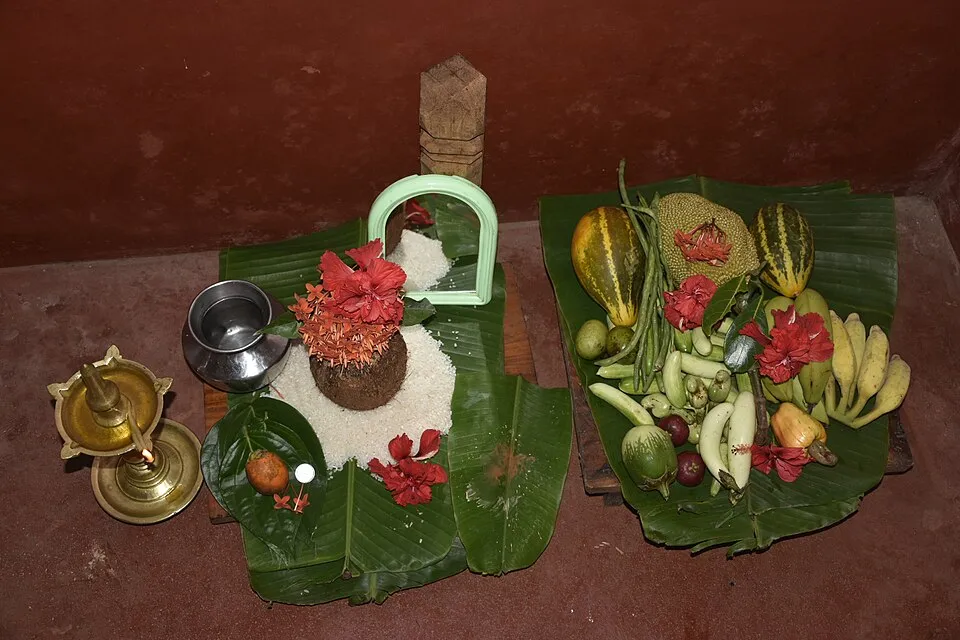 A Bisu kani on banana leaves: a brass lamp, a pot, a coconut with flowers on a heap of rice, a mirror, and a tray of vegetables and fruit