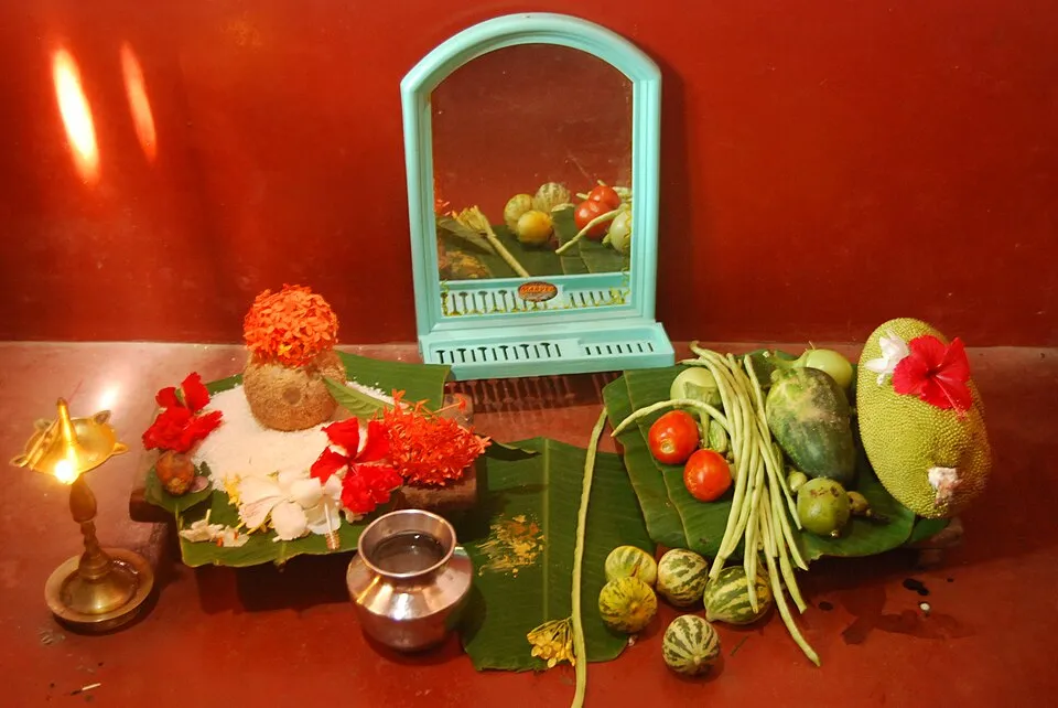 A Bisu kani with a lamp, a pot, a coconut with flowers on rice, a large mirror, and vegetables and a jackfruit on banana leaves