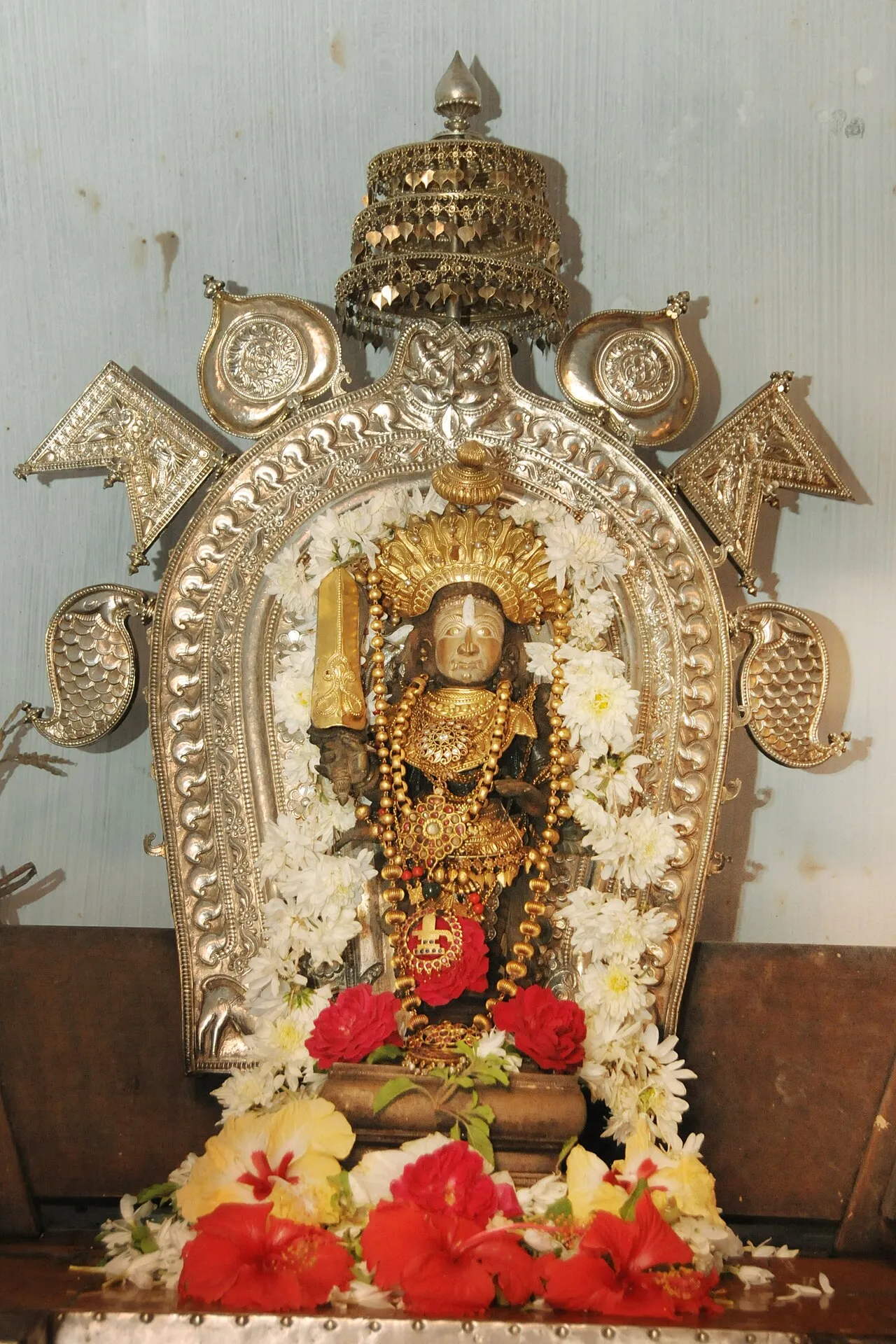 An image of Annappa in a shrine, set in an arched silver frame and decked with red flowers