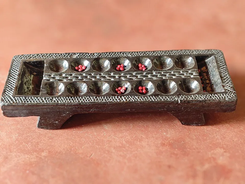 A carved wooden Chennemane board with seeds in the pits