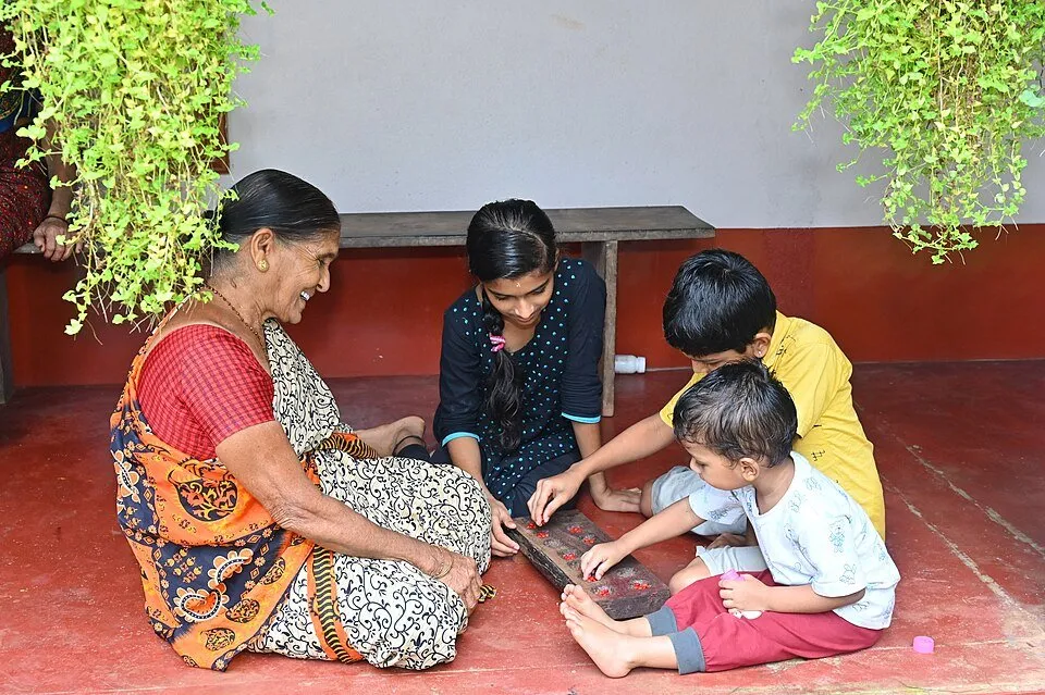 A grandmother playing Chennemane on the floor with three children