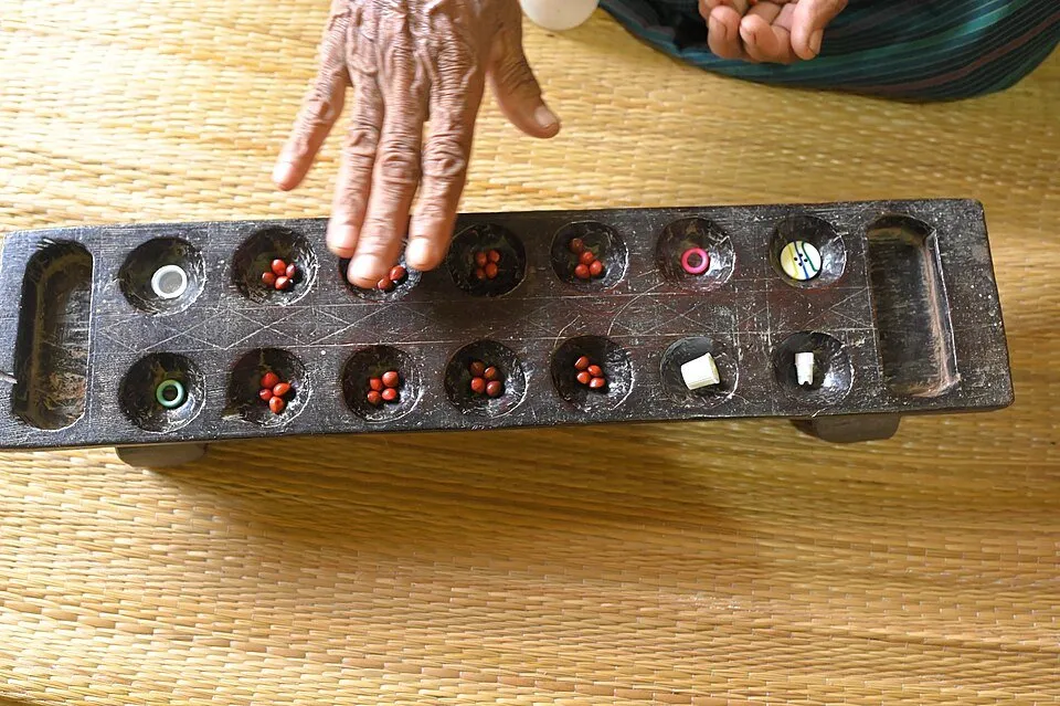 A hand sowing seeds on a Chennemane board