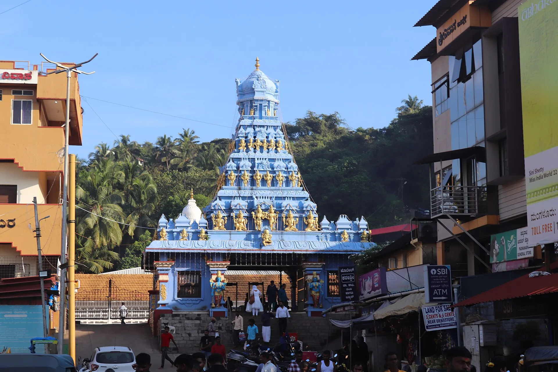 The brightly painted blue entrance tower of the Kadri temple, crowded with carved figures, rising above a busy street