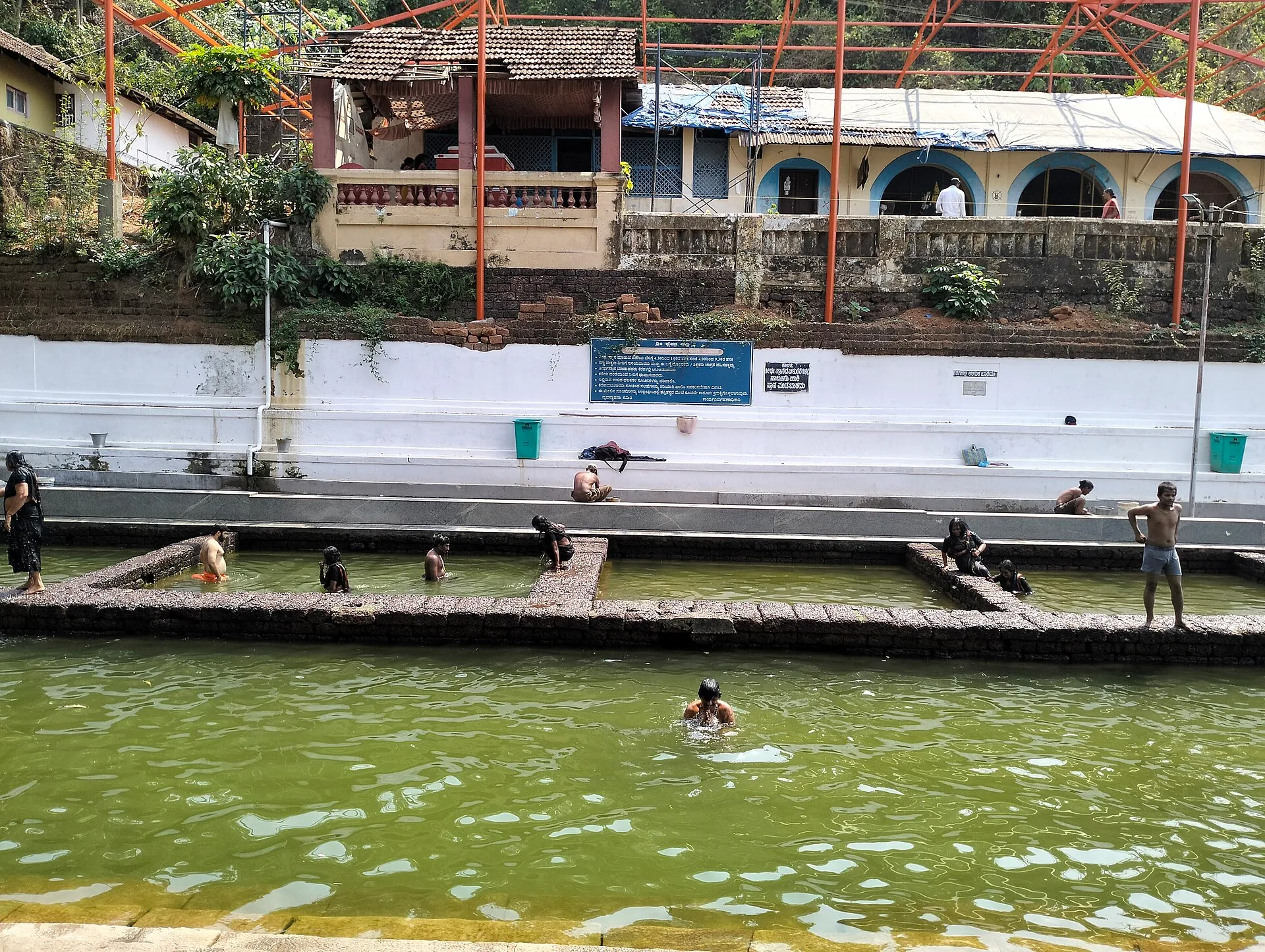 Pilgrims bathing in a stepped temple tank at Kadri, with white walls and buildings above