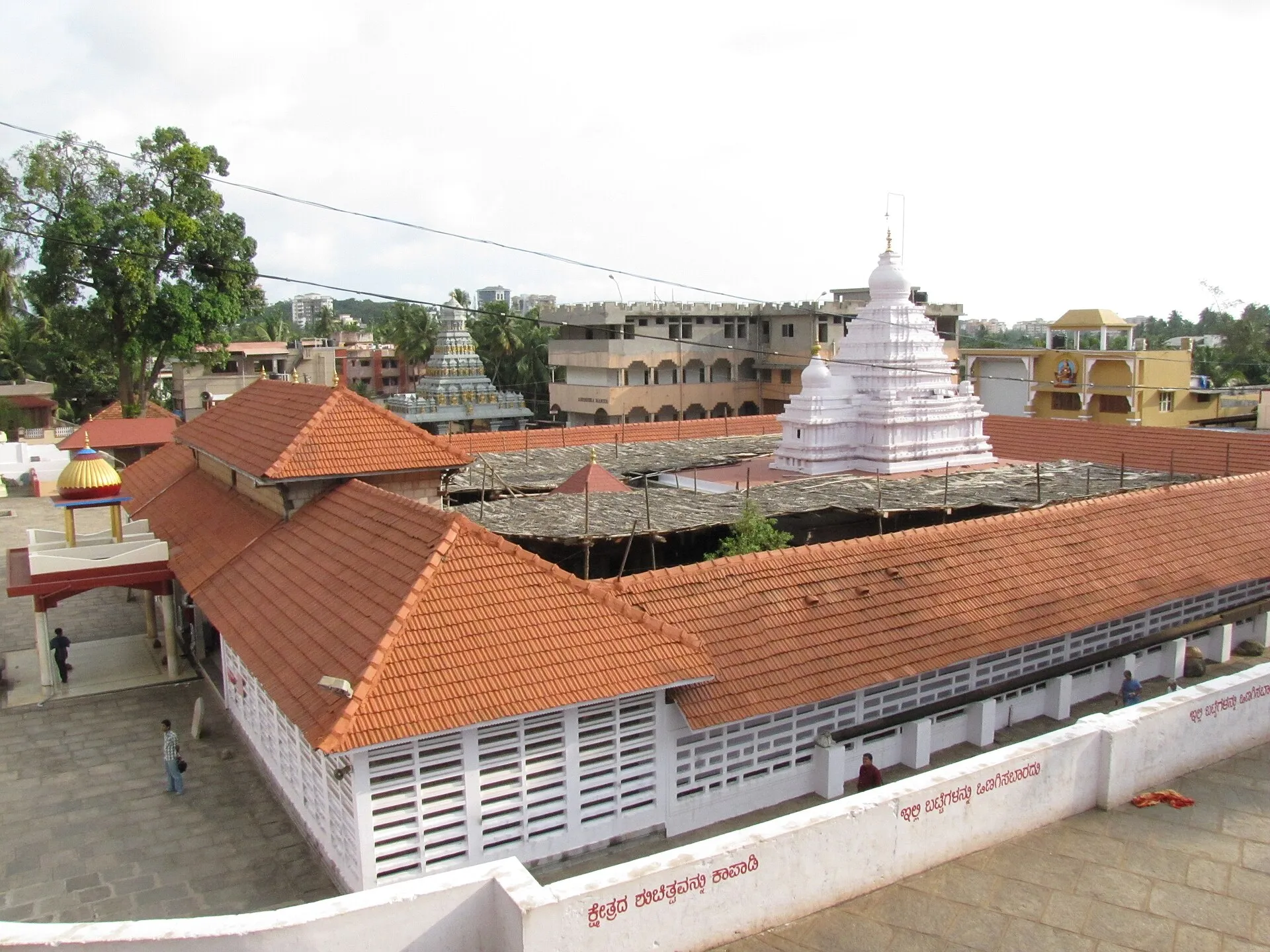 The Kadri Manjunatha temple seen from above: long tiled roofs and white lattice walls around a white tower, with the city beyond