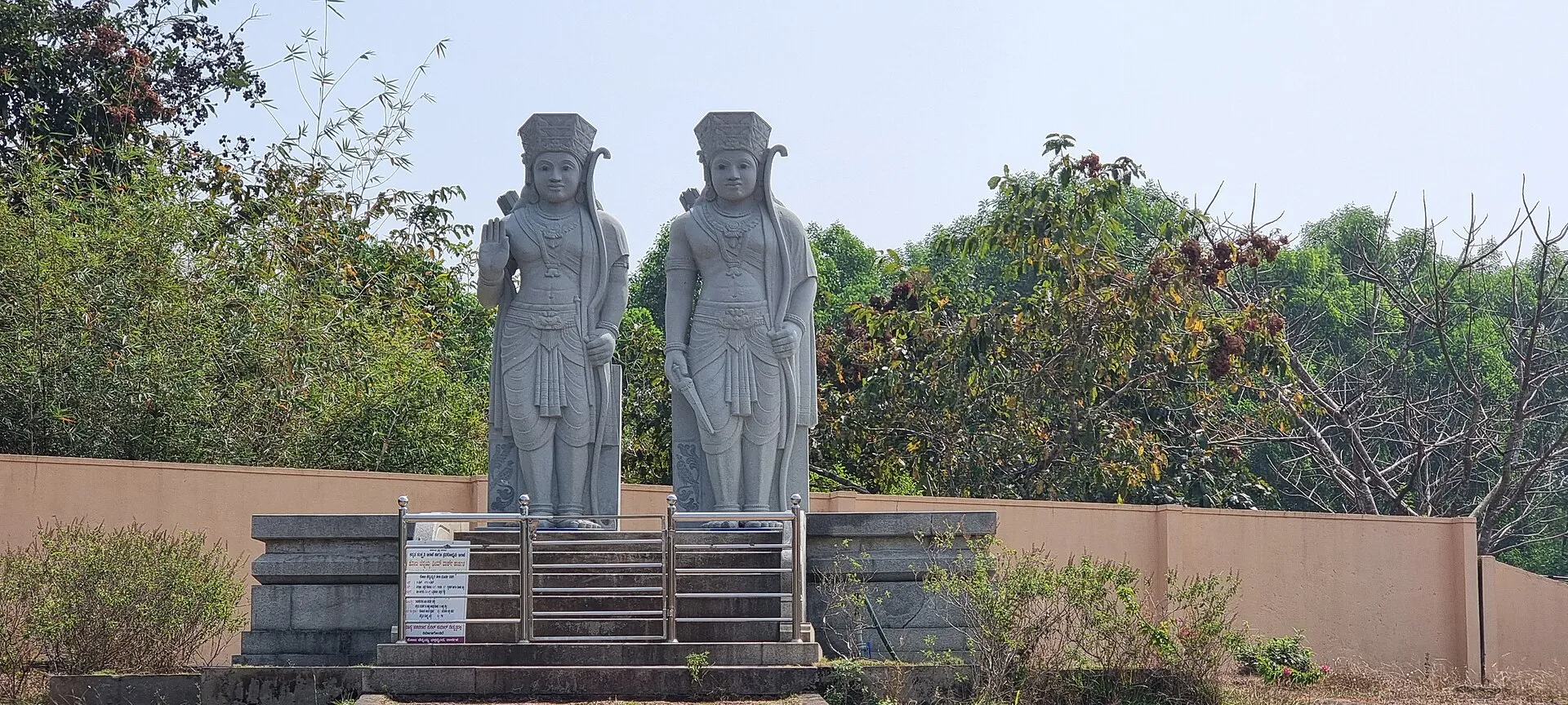 Two tall stone statues of the twin heroes standing side by side on a pedestal among trees