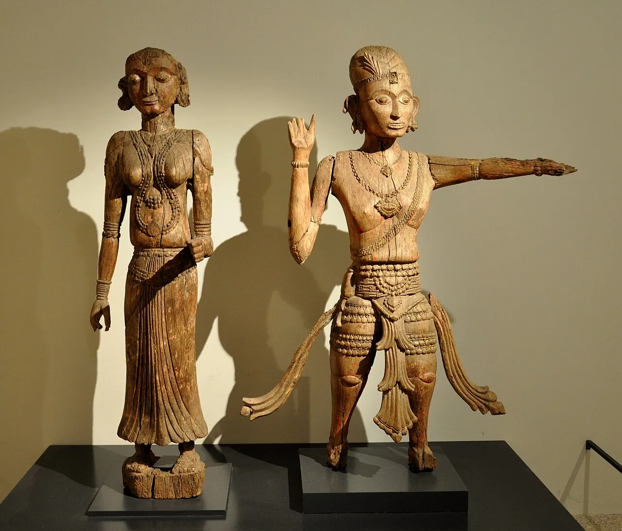 Two carved wooden shrine figures: a woman on the left and a male warrior with an outstretched arm on the right