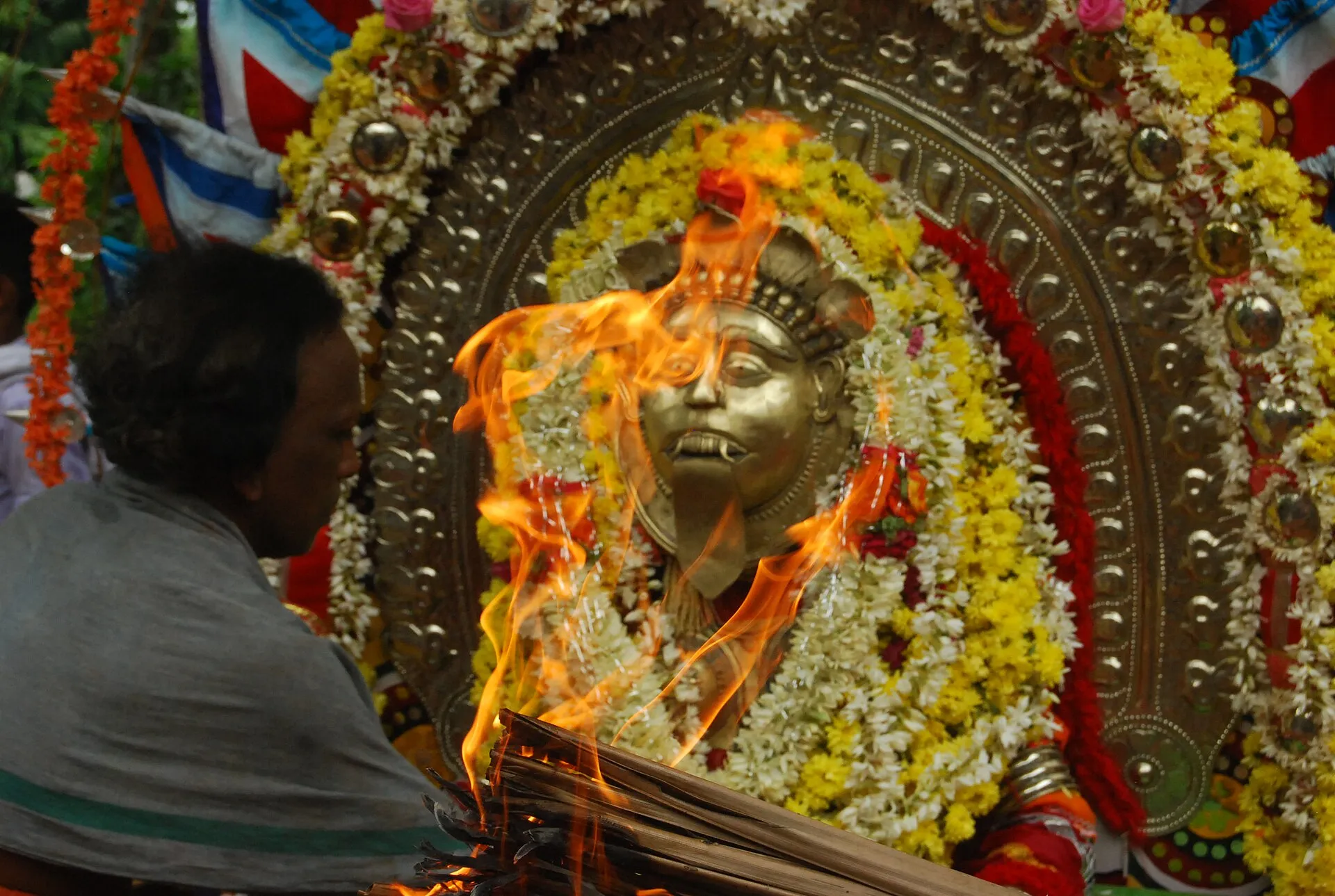 A daiva in full costume and ani, with a burning torch held before its face