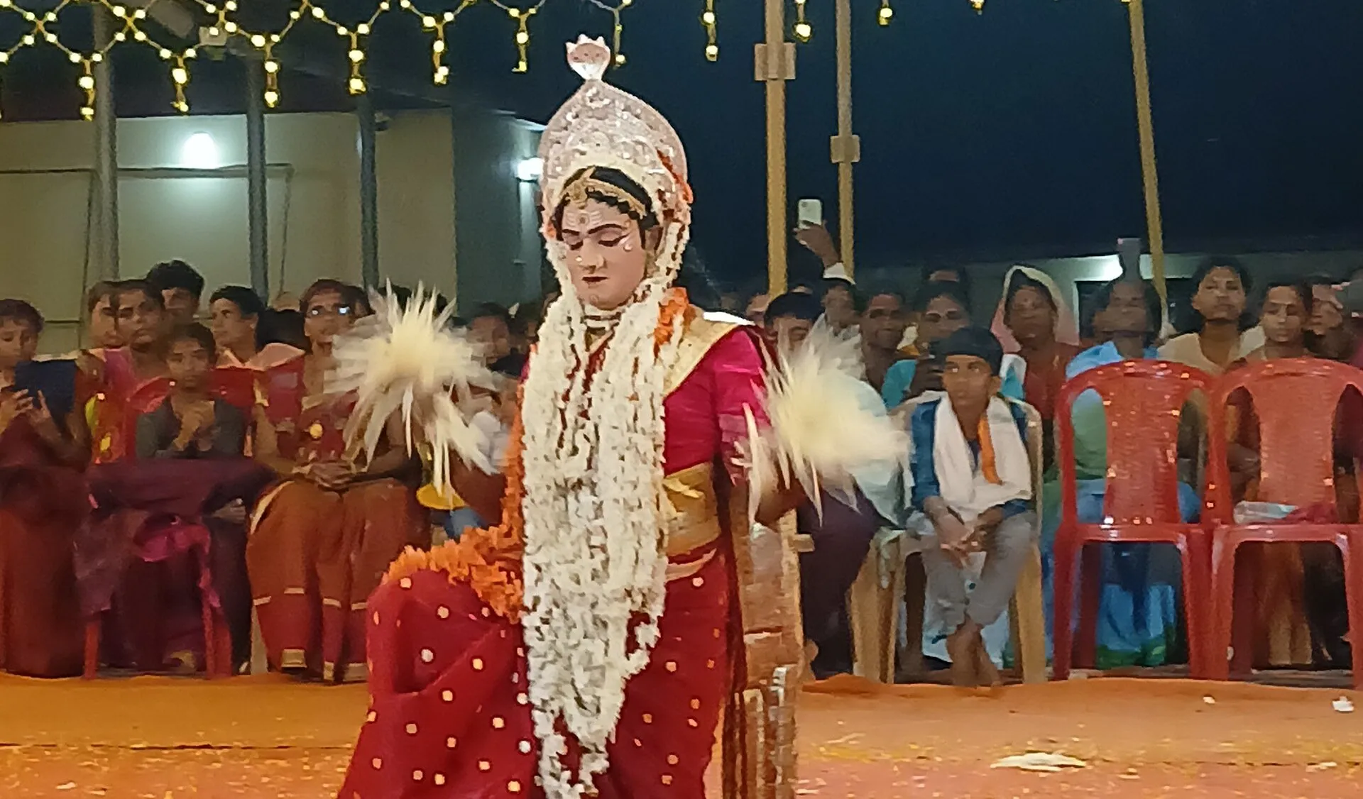 A boy and young girls in the front row watch as the daiva Tannimaniga dances at a night-time kola