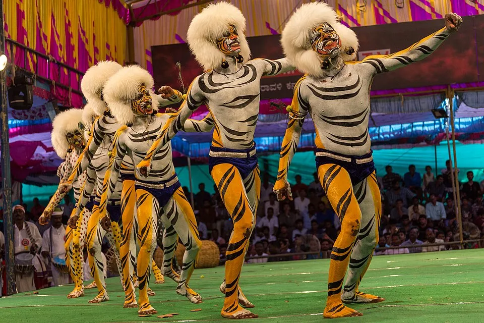 A group of tiger dancers in painted stripes and white fur headpieces on a green stage