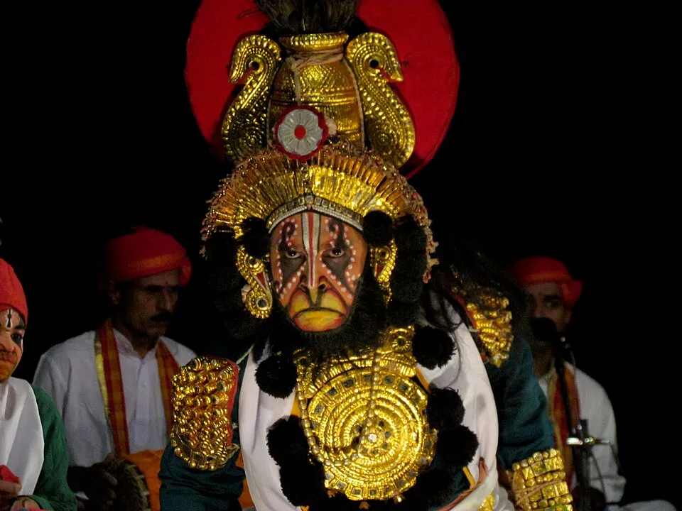 A Yakshagana performer in a gold crown and chest-piece, with musicians in red turbans behind