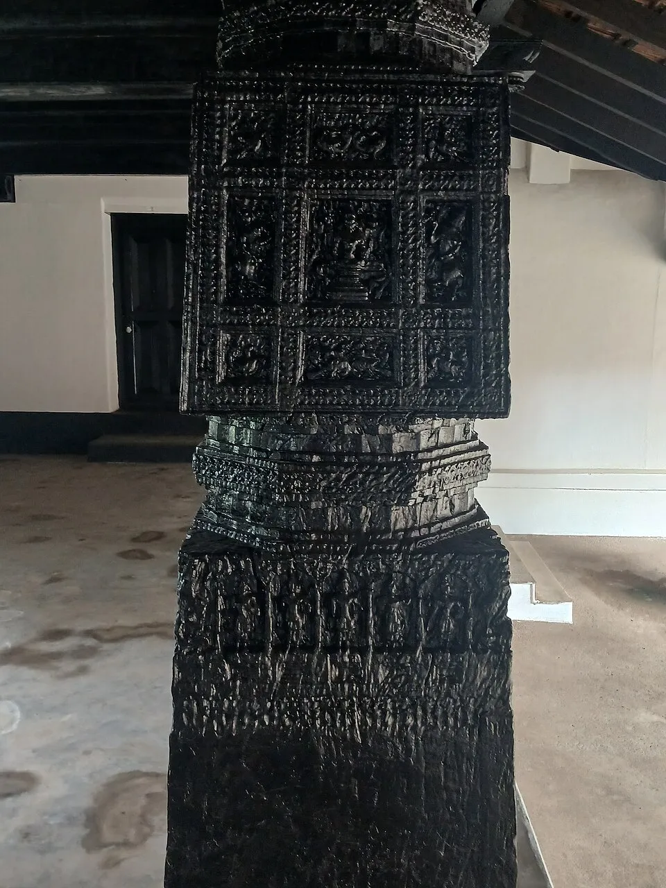 A dark pillar in the Chowta Palace carved all over with small panels of figures