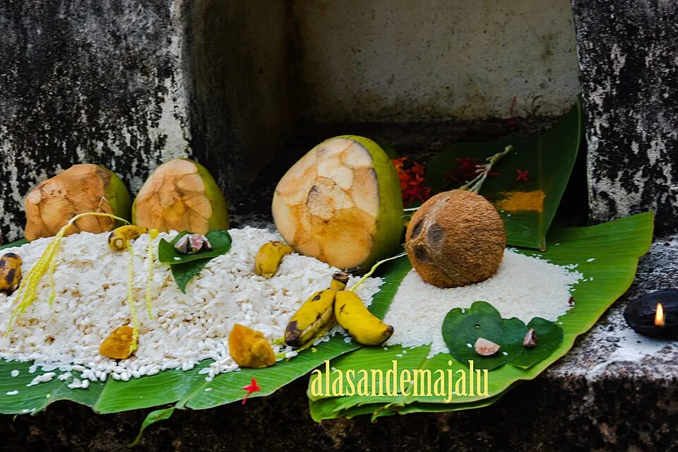 Rice, coconuts and bananas laid out on plantain leaves at a shrine, with a small lamp burning beside them