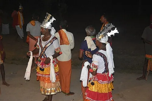 Two performers in tall crowns, white tops and frilled skirts, dancing at night during a Sidda Vesha performance