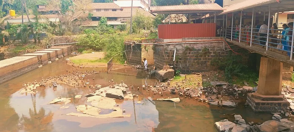 The Nandini river at Kateel, with stepping stones in the shallow water and a covered walkway of the temple beside it