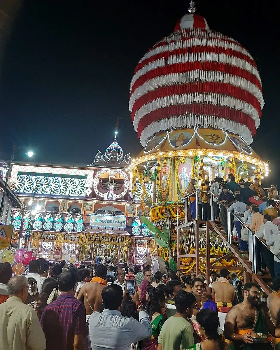The striped chariot and the lit front of the Venkataramana temple at Kodiyal in Mangaluru during the car festival at night, with a crowd of devotees