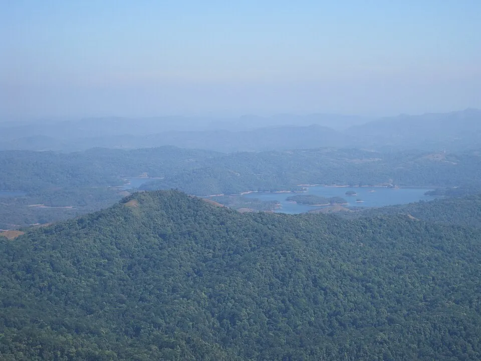 Forested hills of the Kodachadri range in a blue haze, with a reservoir in the valley below