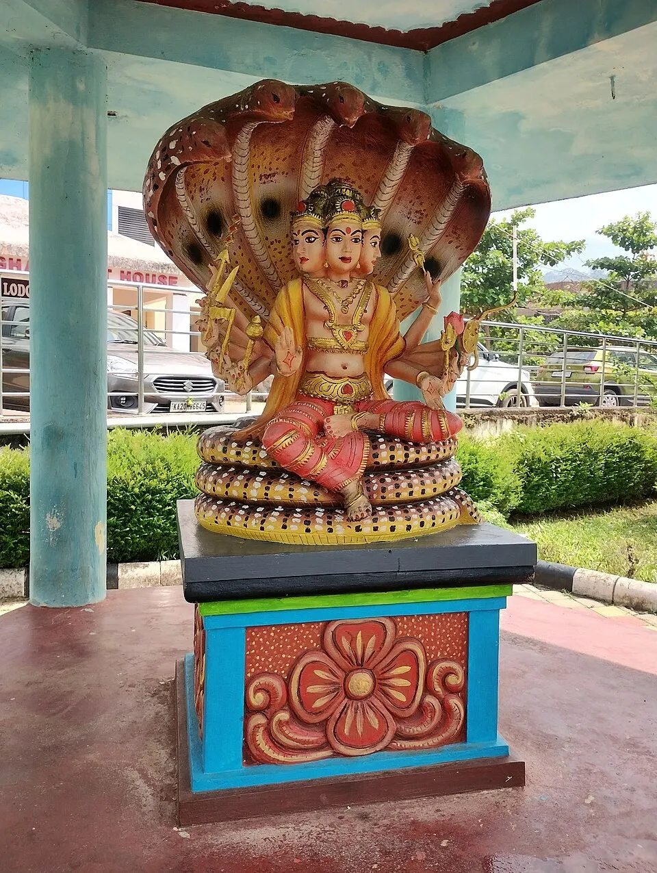 A painted five-hooded serpent sheltering a seated figure, on a decorated pedestal under a roofed pavilion