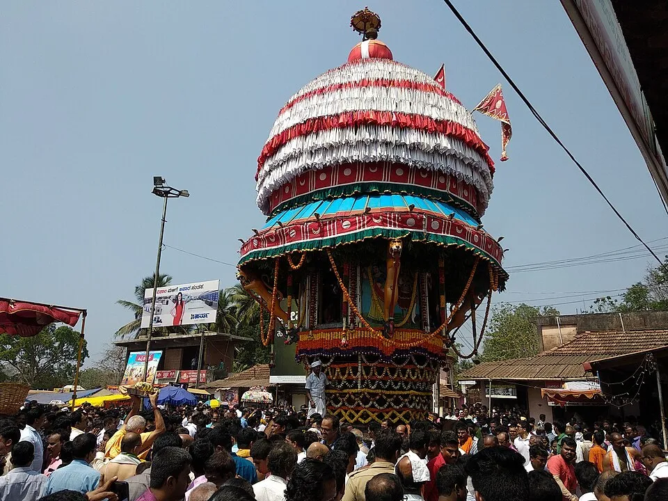 The festival chariot at Mundkur with a white and red decorated dome, among a dense crowd of devotees
