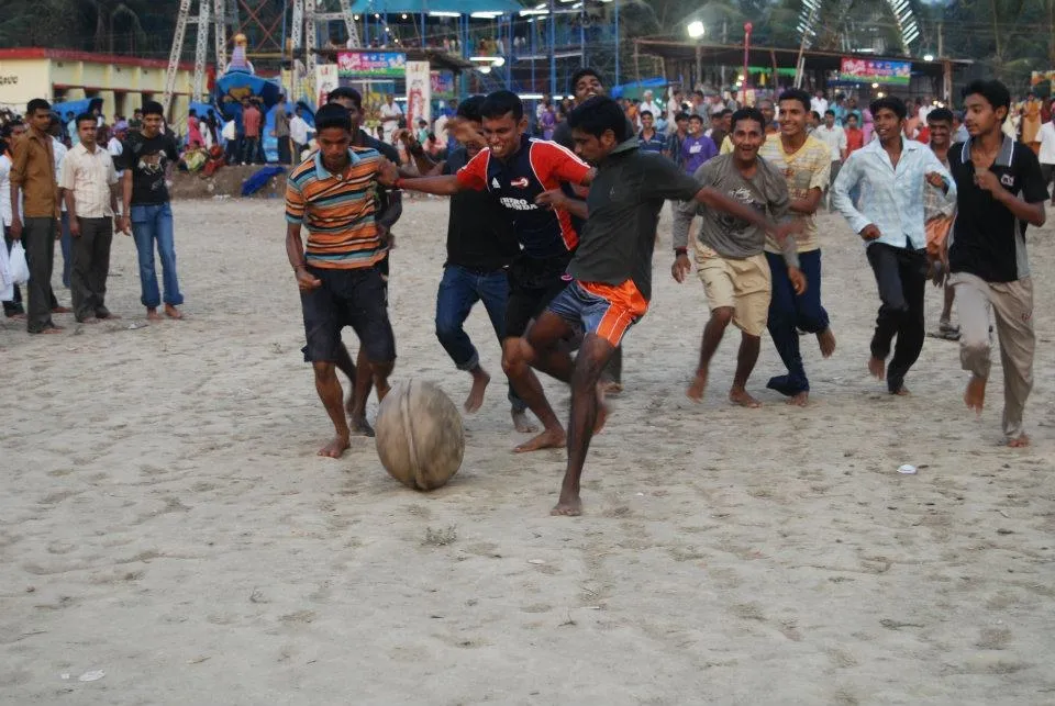 Barefoot men on a sandy ground scrambling for a heavy ball in the Polali Chendu game, with a crowd behind them