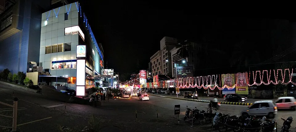 A wide night view of a Mangaluru street strung with red and white lights, with festival banners and traffic