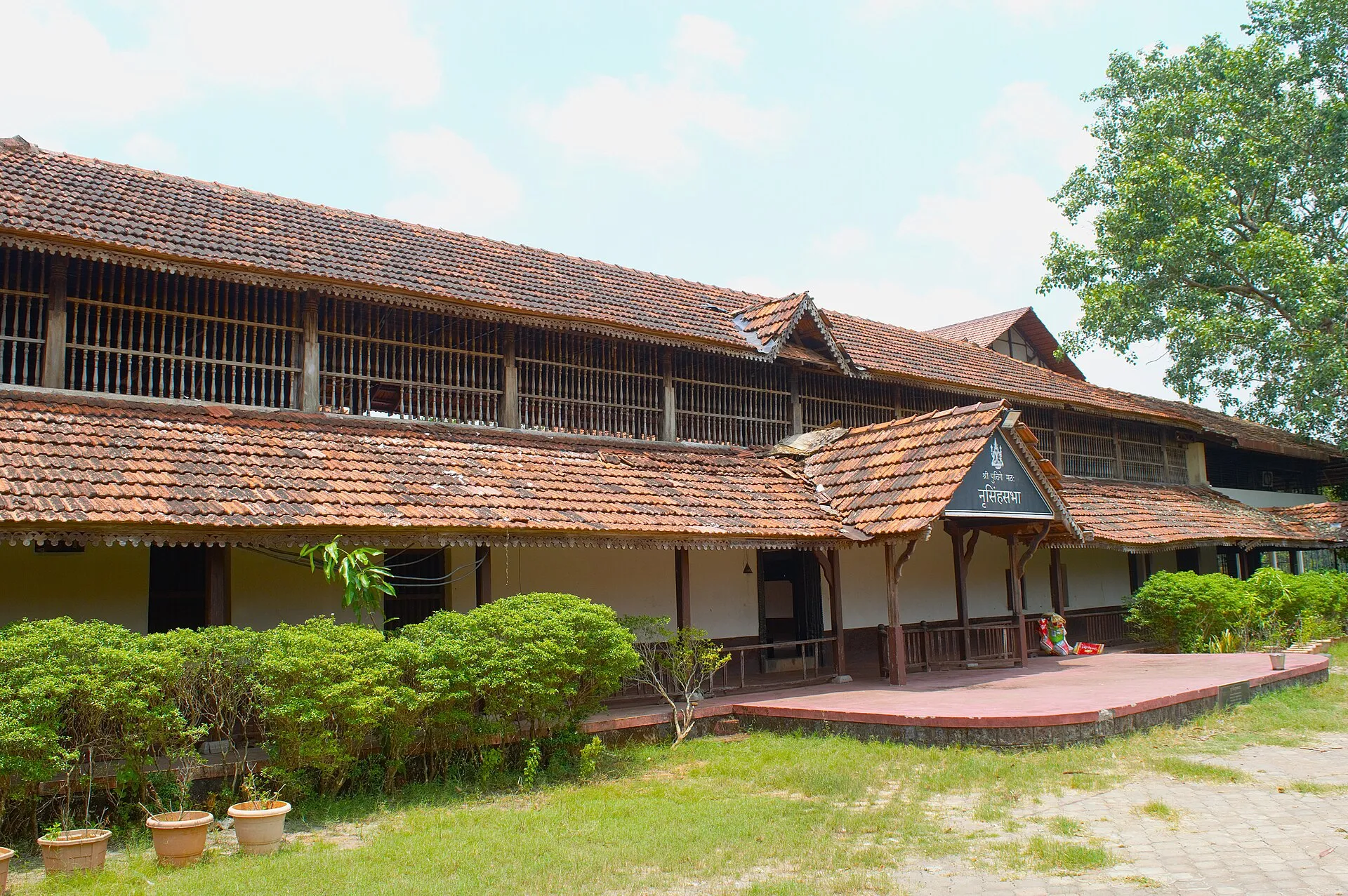 The Puthige moola matha in its home village: a long, low building with a tiled roof behind a garden